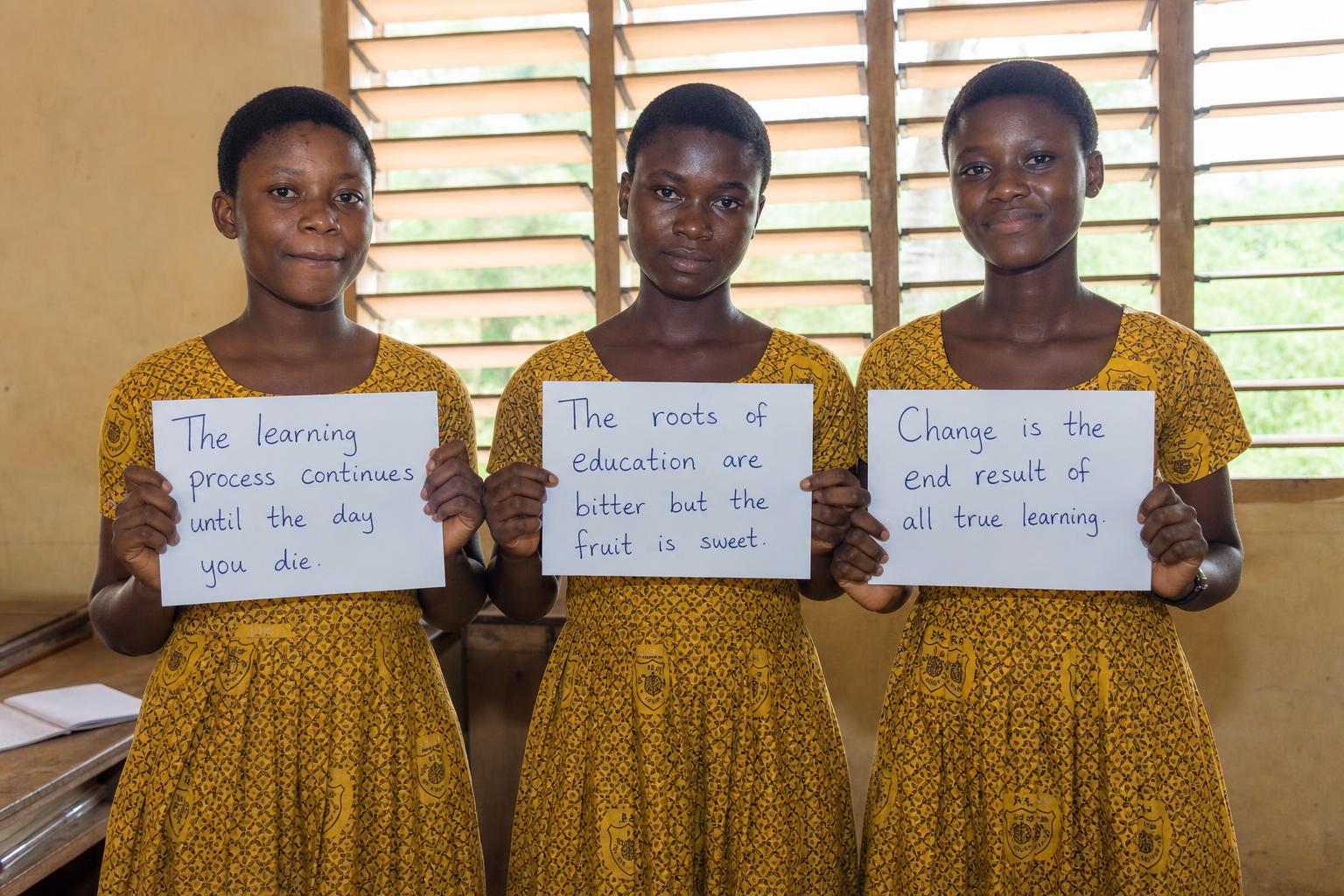 Three Ghanaian schoolgirls holding handwritten signs about education